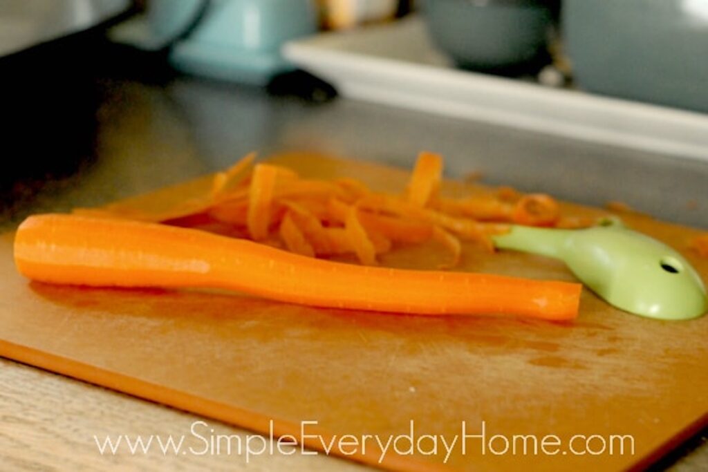 Peeled carrot on a cutting board with green peeler