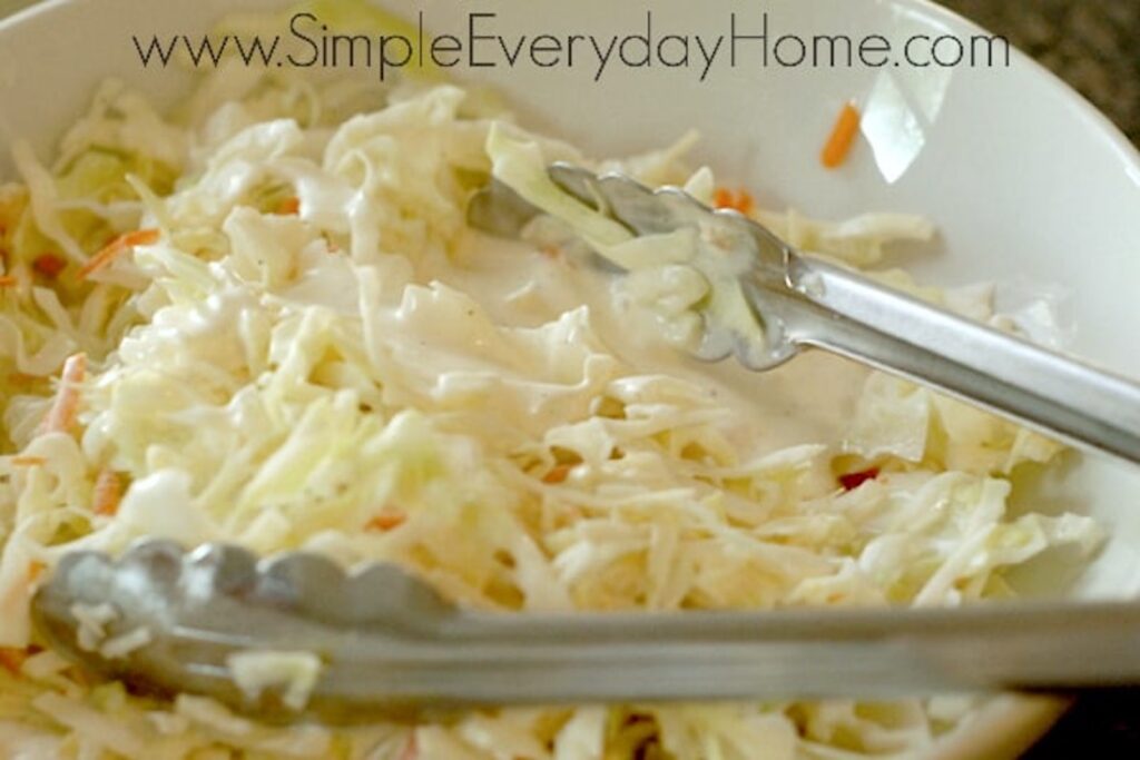 Cole slaw being mixed with dressing with metal tongs