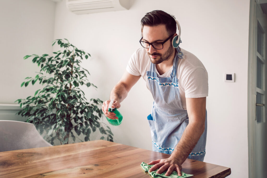 A man spray cleaning a table while wearing an apron