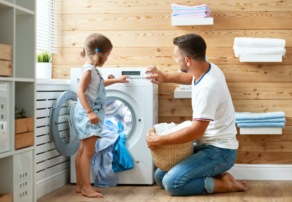 A man and his daughter putting laundry in a washer