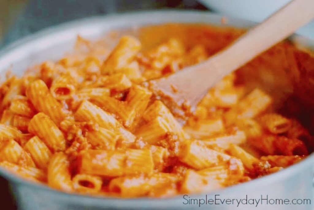 Cooked pasta being stirred into sauce with wooden spoon