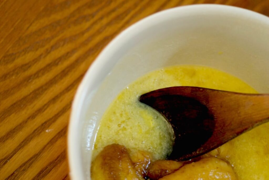 Bowl of eggs being mixed with banana with a wooden spoon