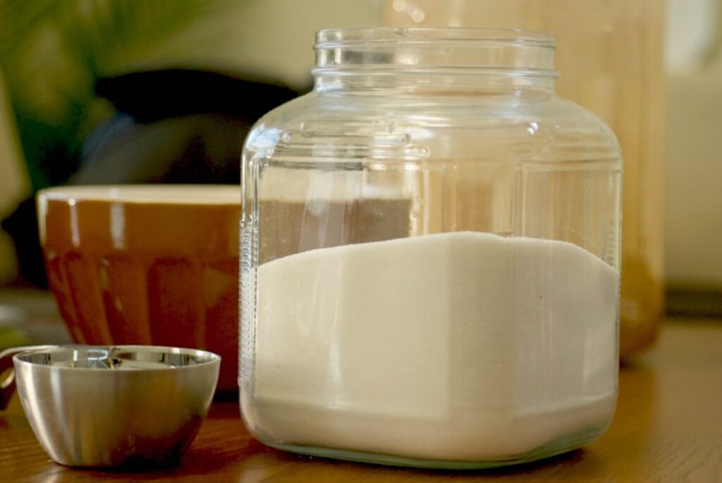 Jar of flour with a measuring cup setting beside it