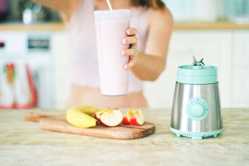 a woman pouring a pink smoothie into a glass with fruit on the counter