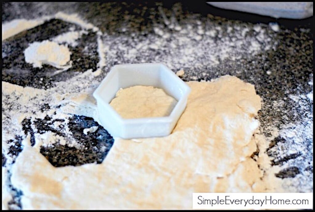 Biscuit dough being cut with plastic cutter on floured counter