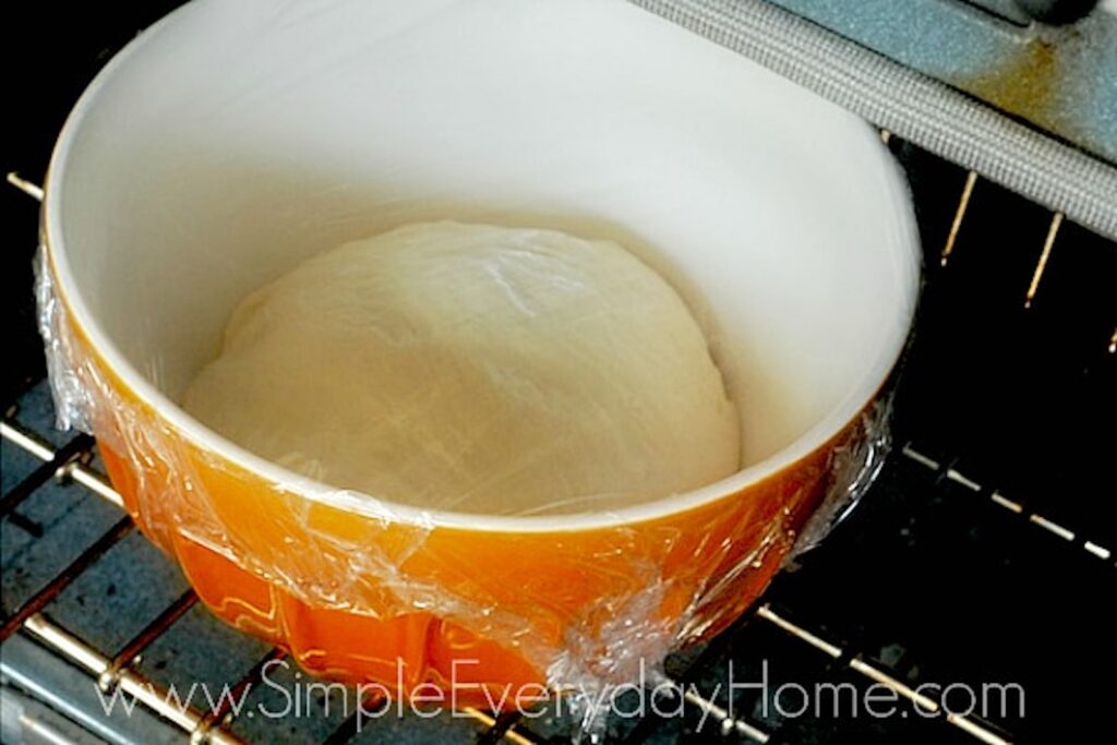 French bread dough in large bowl covered with plastic wrap