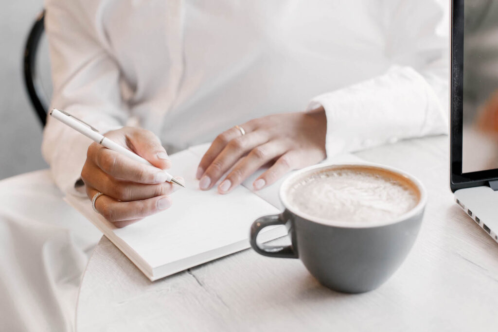 A woman writing in a notebook with a cup of coffee in front of her