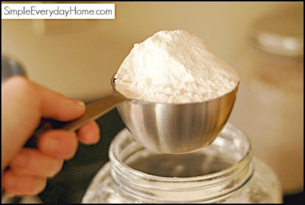 Flour being scooped out of a jar with a measuring cup