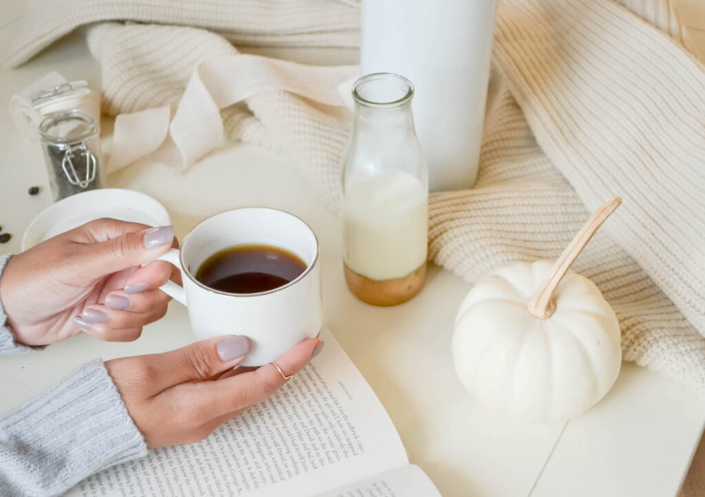 A woman's hands holding a coffee with a book in front of her