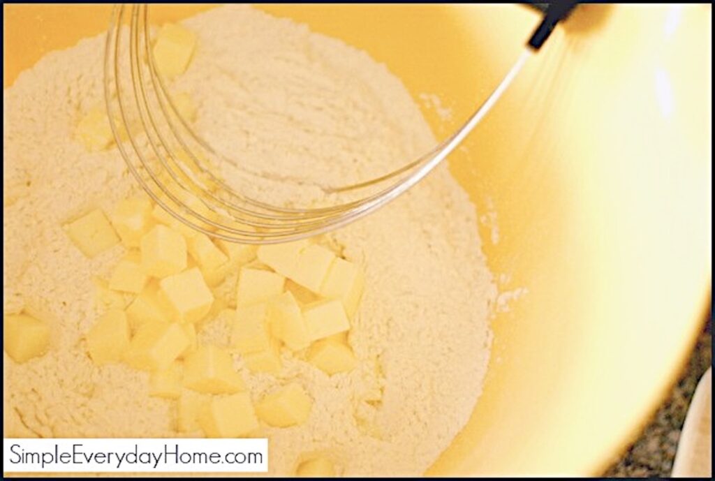 Flour and cubed butter in yellow mixing bowl with pastry cutter