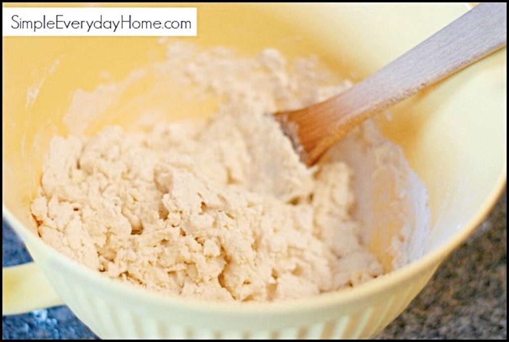 Yellow bowl with biscuit dough being mixed with wooden spoon