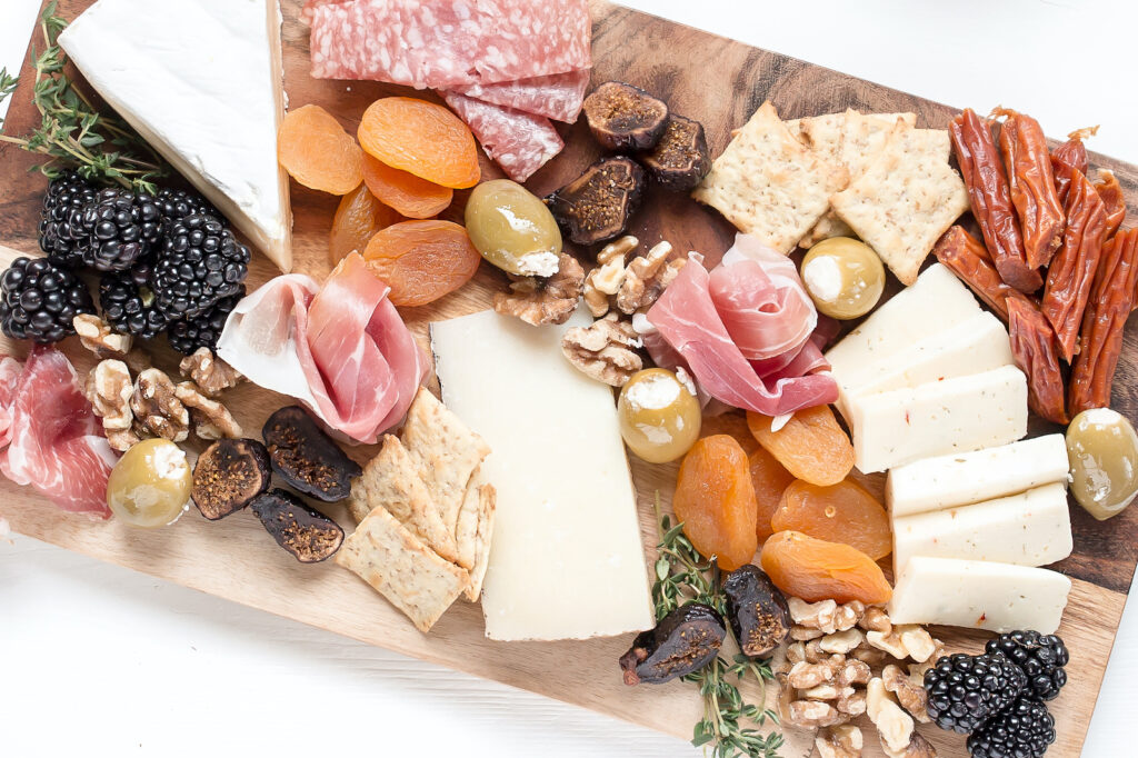 A wooden board with cheese, dried meats, dried fruits, and nuts