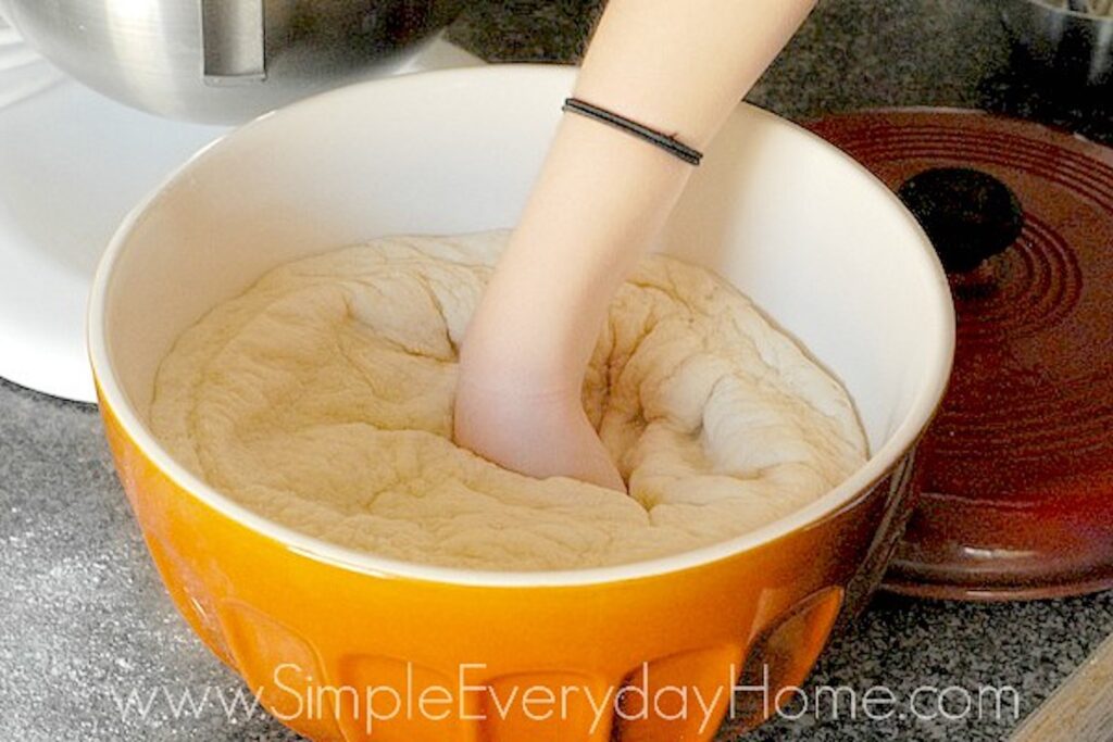 Hand punching down bread dough in bowl
