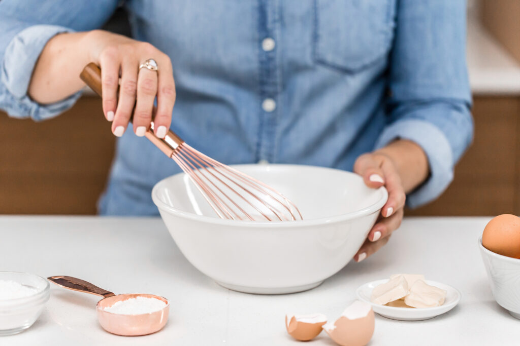 A woman using a coper whisk in a white bowl