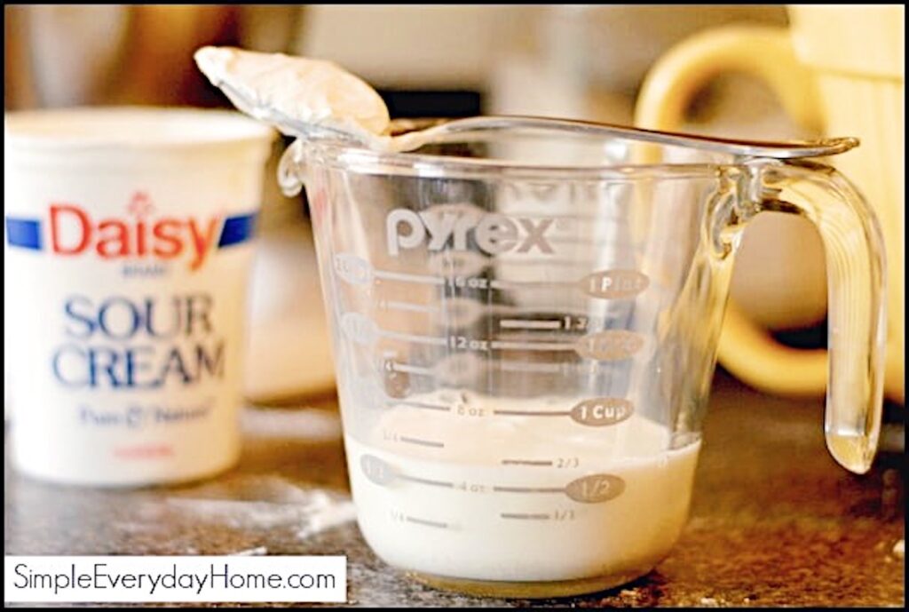 Glass measuring cup with milk in it and a spoon of sour cream setting across the top
