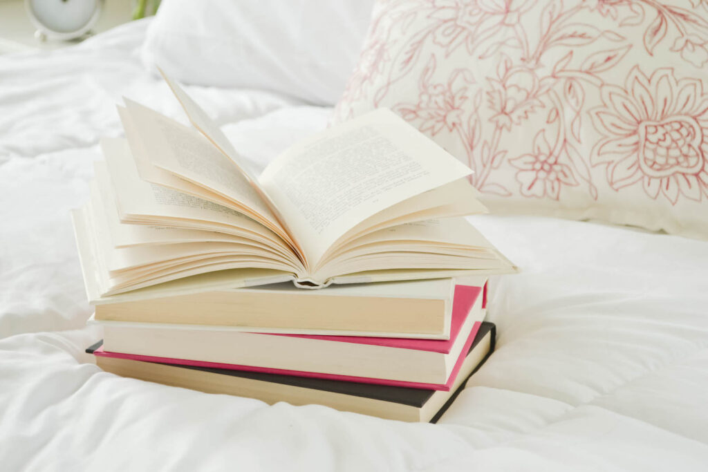 A stack of four books on a pretty white bed