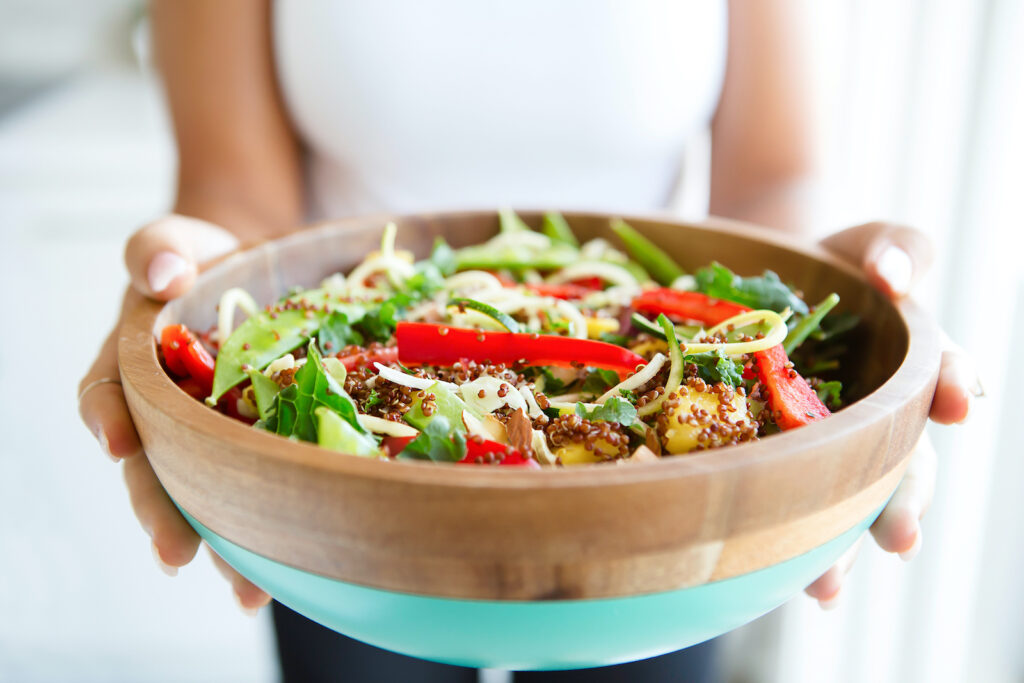 A woman holding out a large bowl with salad in it