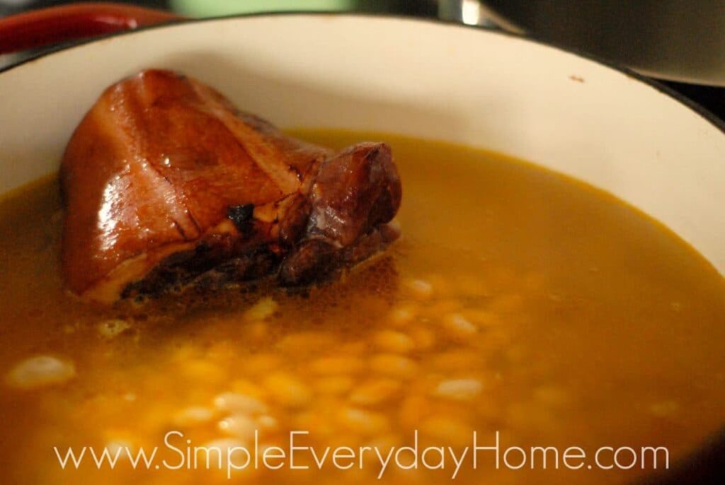 Beans and ham hock covered in broth in Dutch oven