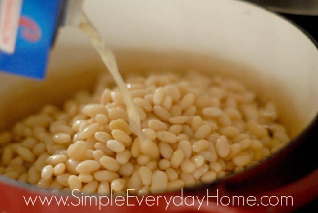 Navy beans in Dutch oven with broth being poured on top